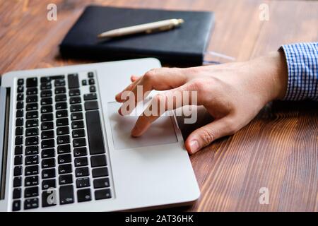 Ein Mann in einem Hemd arbeitet hinter einem Laptop, während er seine Hand auf dem Touchpad führt. Nahaufnahme. Stockfoto