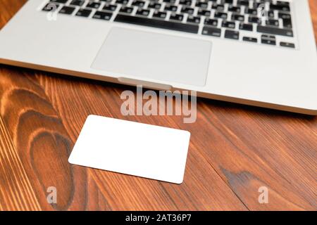 Die Karte verspottete, kopierte Fläche - liegt vor einem Laptop auf einem Holzhintergrund. Nahaufnahme. Stockfoto