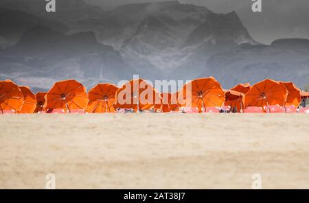 Die Gäste sonnen sich auf Sonnenliegen mit orangefarbenen Sonnenschirmen. Stockfoto