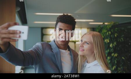 Fröhliche schwarzer Mann mit Lachen, blonde Frau, die selfie mit Smartphone in modernen Büro Spaß haben. Stockfoto