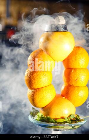 Hookah auf der Orange. Orange Hookah. Hookah mit einem runden durchsichtigen Kolben, in dem in Scheiben geschnittene Orangen und Minzblätter in roter Lauge schweben. Die Kapuzenbuge Stockfoto