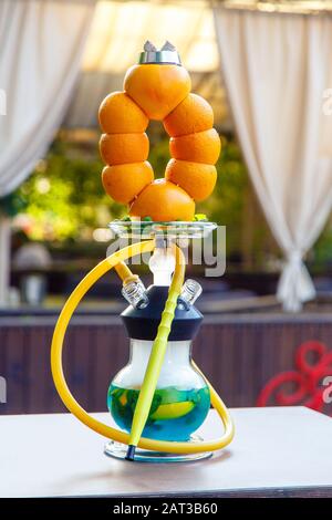Hookah auf Orangen. Citrus Hookah. Hookah mit runder klarer Glühlampe mit rotem Schnaps. Eine Schüssel Hookah aus Orangen. Viel Rauch. Stockfoto