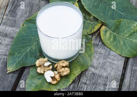 Vegane Muttermilch in einem Glas in der Nähe von Walnüssen auf einem alten Holztisch. Vegane Milch aus Walnüssen. Ökost. Keto trinkt. Stockfoto