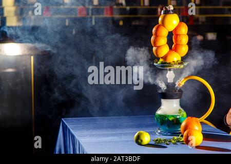 Hookah auf der Orange. Orange Hookah. Hookah mit einem runden durchsichtigen Kolben, in dem in Scheiben geschnittene Orangen und Minzblätter in roter Lauge schweben. Die Kapuzenbuge Stockfoto
