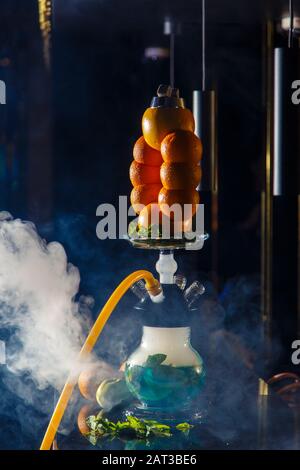Hookah auf der Orange. Orange Hookah. Hookah mit einem runden durchsichtigen Kolben, in dem in Scheiben geschnittene Orangen und Minzblätter in roter Lauge schweben. Die Kapuzenbuge Stockfoto