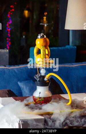 Hookah auf der Orange. Orange Hookah. Hookah mit einem runden durchsichtigen Kolben, in dem in Scheiben geschnittene Orangen und Minzblätter in roter Lauge schweben. Die Kapuzenbuge Stockfoto