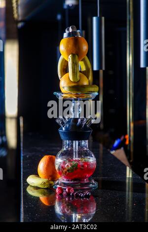 Hookah auf der Orange. Orange Hookah. Hookah mit einem runden durchsichtigen Kolben, in dem in Scheiben geschnittene Orangen und Minzblätter in roter Lauge schweben. Die Kapuzenbuge Stockfoto
