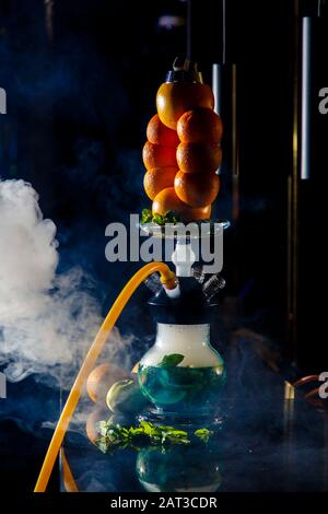 Hookah auf der Orange. Orange Hookah. Hookah mit einem runden durchsichtigen Kolben, in dem in Scheiben geschnittene Orangen und Minzblätter in roter Lauge schweben. Die Kapuzenbuge Stockfoto