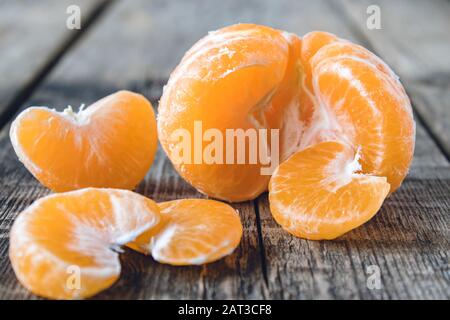 Reif geschälte Tangerine ohne Schale liegt auf dem Tisch neben Stücken reifer Tangerine. Citruszangen oder Orangen. Nahaufnahme. Stockfoto