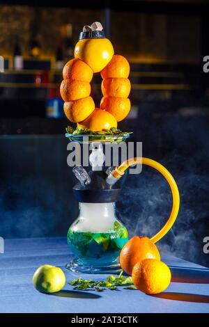 Hookah auf der Orange. Orange Hookah. Hookah mit einem runden durchsichtigen Kolben, in dem in Scheiben geschnittene Orangen und Minzblätter in roter Lauge schweben. Die Kapuzenbuge Stockfoto