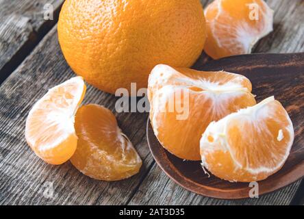 Scheiben reifer gelber Mandarinen liegen in einer Schüssel nahe einer ganzen Mandarine auf einem Holztisch. Zitrusfrüchte, Mandarinen oder Orangen. Nahaufnahme. Stockfoto