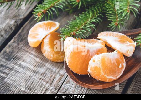 Reife geschälte Scheiben von Tangerin ohne Schale liegen in einer Schüssel auf dem Tisch neben Stücken gelber Tangerine und neben grünen Zweigen eines Weihnachts-t Stockfoto