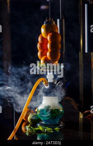 Hookah auf der Orange. Orange Hookah. Hookah mit einem runden durchsichtigen Kolben, in dem in Scheiben geschnittene Orangen und Minzblätter in roter Lauge schweben. Die Kapuzenbuge Stockfoto