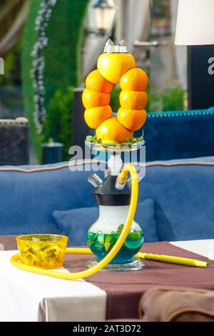 Hookah auf der Orange. Orange Hookah. Hookah mit einem runden durchsichtigen Kolben, in dem in Scheiben geschnittene Orangen und Minzblätter in roter Lauge schweben. Die Kapuzenbuge Stockfoto