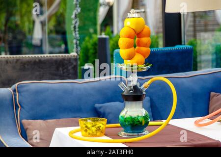 Hookah auf der Orange. Orange Hookah. Hookah mit einem runden durchsichtigen Kolben, in dem in Scheiben geschnittene Orangen und Minzblätter in roter Lauge schweben. Die Kapuzenbuge Stockfoto