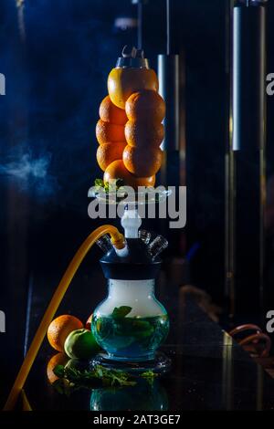 Hookah auf der Orange. Orange Hookah. Hookah mit einem runden durchsichtigen Kolben, in dem in Scheiben geschnittene Orangen und Minzblätter in roter Lauge schweben. Die Kapuzenbuge Stockfoto