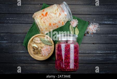 Glasgefäße aus fermentiertem Weiß, Rotkohl, Gewürzen, Salz. Gemüse auf dunklem Hintergrund. Mit Textilgrün. Fermentation ist eine Quelle für Probiotika Stockfoto