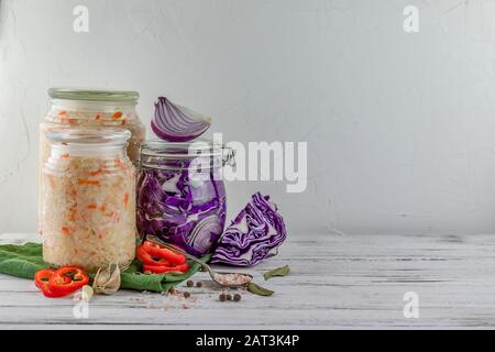 Drei Glasgefäße aus fermentiertem Weiß, Rotkohl, Zwiebeln, Pfeffer, Gemüse auf hellem Hintergrund. Mit Textilgrün. Fermentation ist eine Quelle von p Stockfoto