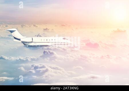 Mittelgroßer moderner vip-Privatjet, der bei warmem, farbenfrohem Sonnenuntergang hoch in den Himmel fliegt und über den lauschigen, lockigen Wolken am Abend flieht. Luxus kleine Unternehmen Stockfoto