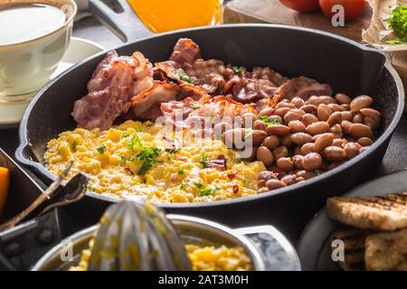 Komplettes englisches Frühstück. Rührei gegrillte Speckbohnen Toast Brot Orangensaft und Kaffee Stockfoto
