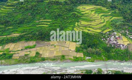 Dorf und Fluss in einer Bergschlucht, Draufsicht. Reisanbau im Norden der Philippinen, Luftbild. Tropische Landschaft, Fluss- und Reisfelder. Landschaft, Dörfer im Hochland. Stockfoto