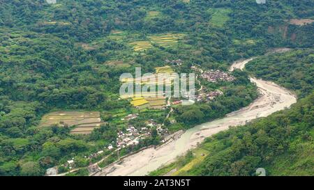 Dorf und Fluss in einer Bergschlucht, Draufsicht. Reisanbau im Norden der Philippinen, Luftbild. Tropische Landschaft, Fluss- und Reisfelder. Landschaft, Dörfer im Hochland. Stockfoto