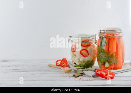 Zwei Glasgefäße aus fermentiertem Blumenkohl, Karotten, Gemüse auf hellem Hintergrund. Mit Textilhellgrau. Fermentation ist eine Quelle für Probiotika. Stockfoto