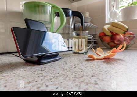 Kabelloses Aufladen des Smartphones auf der Ladestation auf der Tischplatte in der Küche. Stockfoto