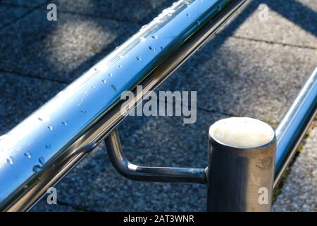 Rollstuhl mit Betonfliesen und Handicap-Rampe. Handlauf aus Edelstahl im selektiven Fokus. Verschwommener grauer Hintergrund. Barrierefreies Zugangskonzept. Stockfoto