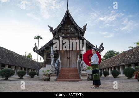 Eine asiatische Frau in chiang Mai Thailand steht in einem roten Regenschirm mit einer Kulisse eines alten Tempels. Stockfoto