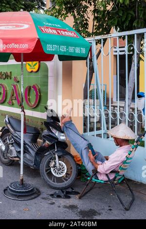 Mann saß im Stuhl und schaute mit den Füßen hoch auf dem Motorrad, Ho-Chi-Minh-Stadt, Vietnam Stockfoto