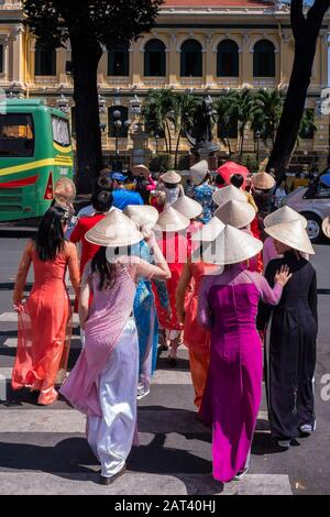 Junge Frauen, die sich in Ao Dai bekleidet haben, überqueren die Straße in Richtung Central Post Office, Ho-Chi-Minh-Stadt, Vietnam Stockfoto