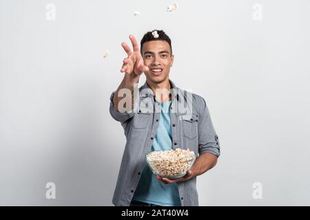 Mulatto man hält einen Teller Popcorn in den Händen und wirft Popcorn auf die Kamera Stockfoto