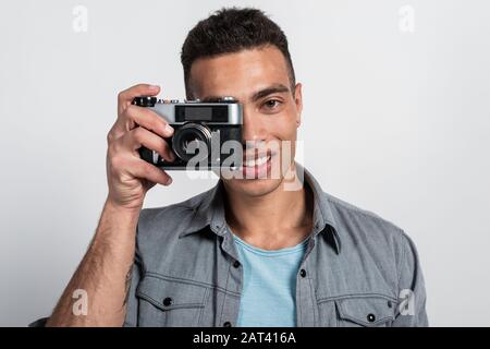 Lächelnder Mulatto-Mann, der eine Retro-Photokamera gegen sein Gesicht hält und das Kamerabild betrachtet Stockfoto