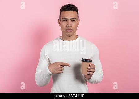 Schlafender Kerl, der ein Papierglas Kaffee hält und müde darauf zeigt.- Bild Stockfoto