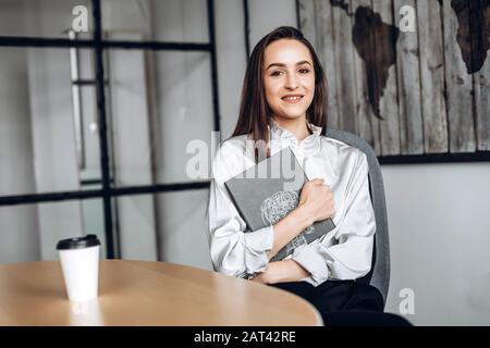 Hübsches Brunette mit Dokumenten in ihr und Tassen Kaffee, Arbeit im Beamten Stockfoto