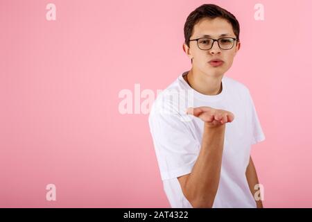 Glücklich in der Liebe ein gutaussehender junger Mann in einer Brille, die steht und die Kamera betrachtet und Luftkuss sendet Stockfoto