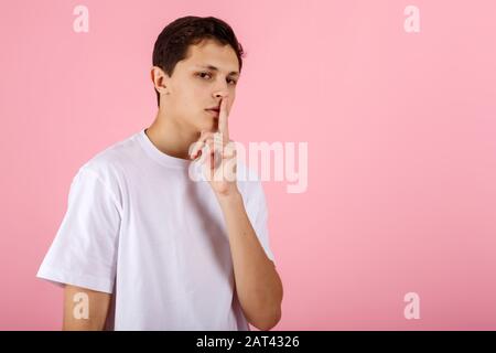 Guy in einem weißen T-Shirt legt seinen Finger auf die Lippen und zeigt ein Zeichen der Stille Stockfoto