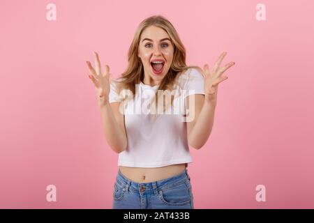 Bild einer aufgeregt schreienden jungen Frau, die über rosafarbenem Hintergrund steht. Aussehende Kamera. Stockfoto
