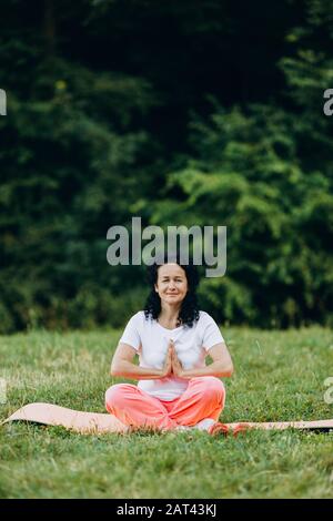 Seniorin, die im Yoga sitzt, posieren auf Yogamatte und machen Geste namaste.- - Bild Stockfoto