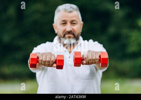 Älterer Mann, der eine Hanteln in geraden Händen hält. Hanteln im Fokus - Bild Stockfoto