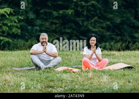 Frau im mittleren Alter und Mann, die im Freien Yoga machen und dabei Geste namaste machen.- Bild Stockfoto