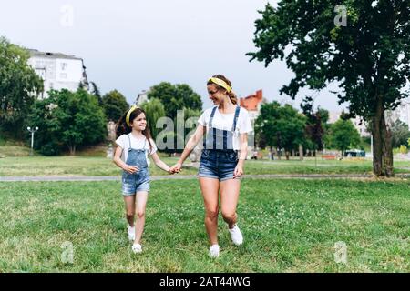 Glückliche Mutter und Tochter, die Hand an Hand halten und sich gegenseitig im Freien sehen.- Konzeptfamilie Stockfoto