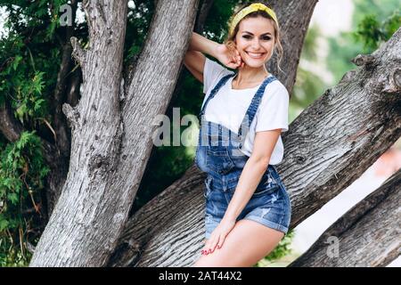 Horizontales Porträt einer glücklichen Frau, die sich an einen Baum im Freien lehnt.- Bild Stockfoto