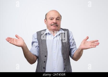 Der fraglos zweifelhafte, unzufriedener Senior zuckt sich unbestimmt mit den Schultern, weiß nicht, wie sich das zukünftige Leben verändert oder was zu tun ist. Studio-Foto. Stockfoto