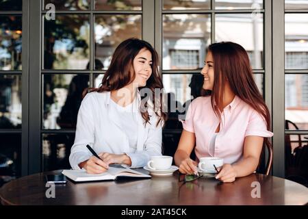 Die Mädchen, die im Café arbeiten, schreiben wichtige Thesen im Notizbuch auf Stockfoto