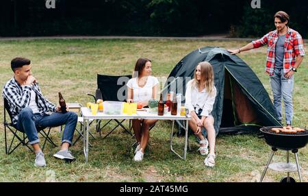 Junge Kerle im Camping neben einem Zelt haben ein Mittagessen und haben eine lustige Zeit Stockfoto