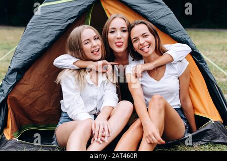 Hübsche Mädchen umarmen und zeigen eine Zunge, die im Zelt sitzt. - Konzept Camping Stockfoto