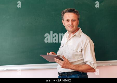 Mittelalterslehrer neben der Tafel, die ein ipad hält, und erklären Sie eine Lektion.- Bild Stockfoto