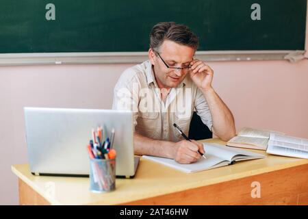 Lächelnder Mittelalterslehrer in der Brille schreibt aufmerksam .- Bild Stockfoto